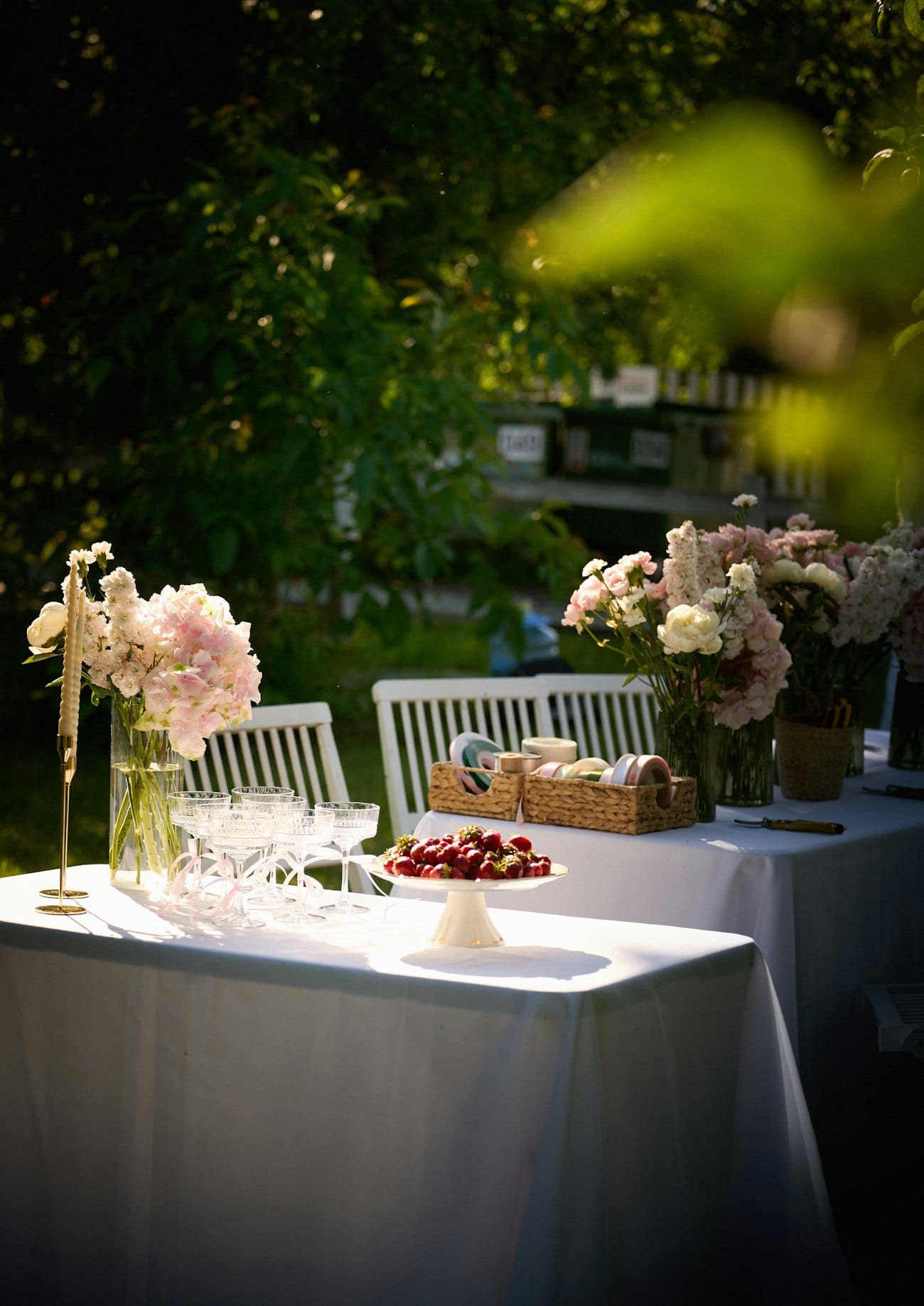 Tables nappées de blanc dressées en jardin avec fleurs et coupes